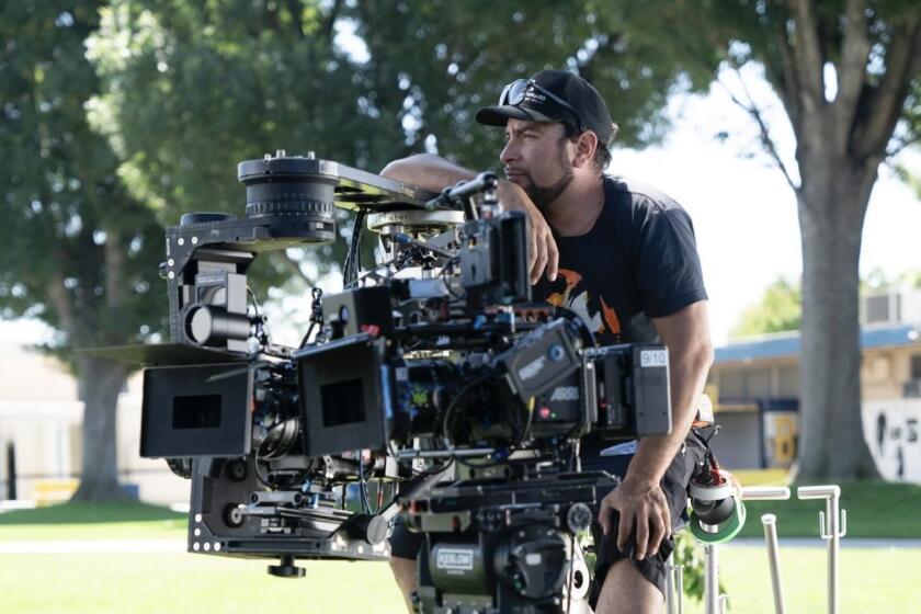 Diego Mariscal, in a black cap and T-shirt, sits on a camera dolly.