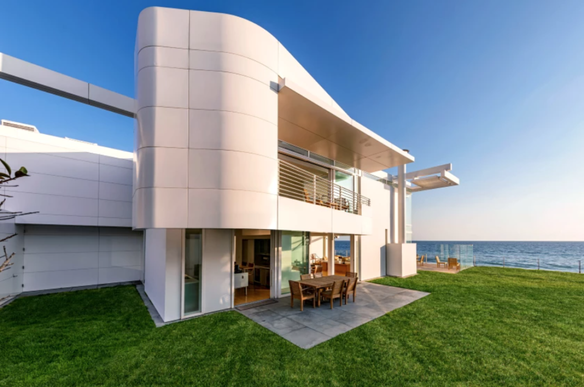 A modern home with aluminum panels has a rectangular patio and deep green lawn.