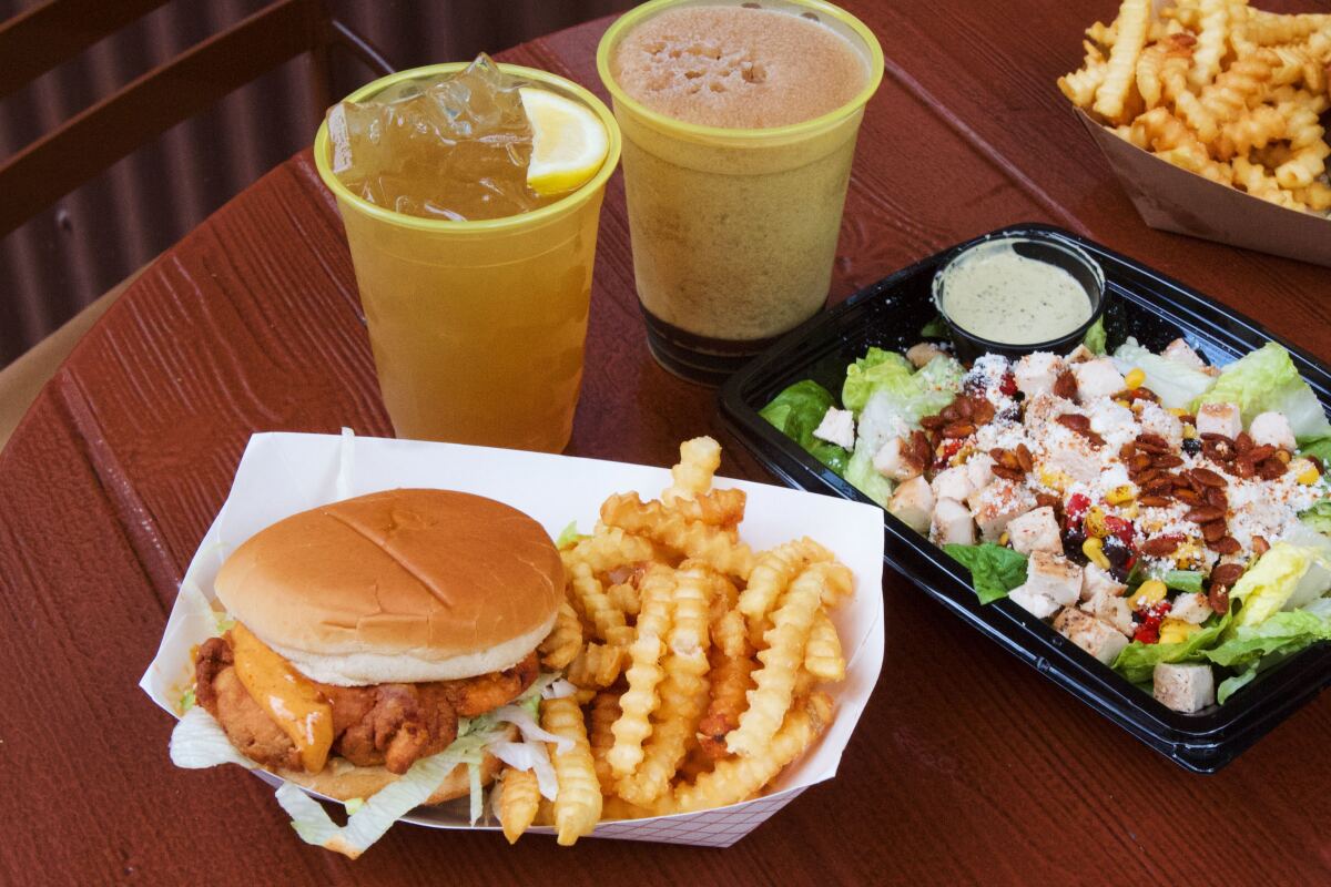 A table of food including fried chicken sandwich and salad, plus bourbon sweet tea lemonade and a frozen whiskey Coke.