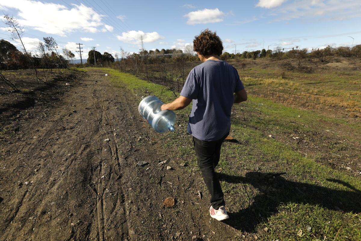 A person carries an empty water jug down a dirt path