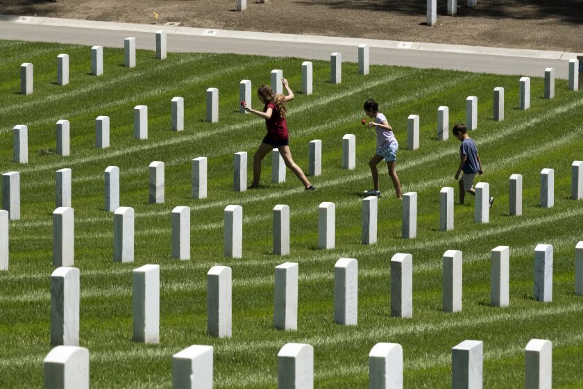 Children place a flowers at the graves of fallen soldiers to pay their respects during Memorial Day observances at the Los Angeles National Cemetery to honor fallen soldiers and health care workers in Los Angeles, Monday, May 25, 2020. The annual Memorial Day commemoration at the cemetery was held without the public in attendance due to the coronavirus outbreak. (AP Photo/Richard Vogel)