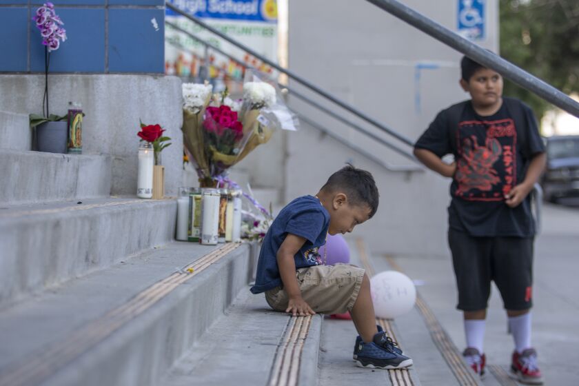 Los Angeles, CA - September 16: Joaquin Kuripeth, 3, left, and Nelson Kuripeth, 10, right, wait outside the school for their sibling to come out of class next to a memorial on the steps outside on Friday, Sept. 16, 2022, in the Hollywood neighborhood of Los Angeles, CA. Their mother said their father died of covid and it was hard on the children to see the memorial. Two high school boys were arrested Thursday, one on suspicion of manslaughter for allegedly selling what is believed to be a fentanyl-laced pill that led to the overdose death of a student at Helen Bernstein High School. Authorities said that the student was found in a bathroom at the Hollywood school this week. (Francine Orr / Los Angeles Times)