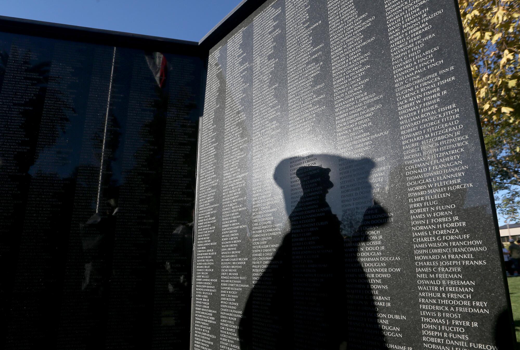 A man's shadow on a black marble memorial with names inscribed