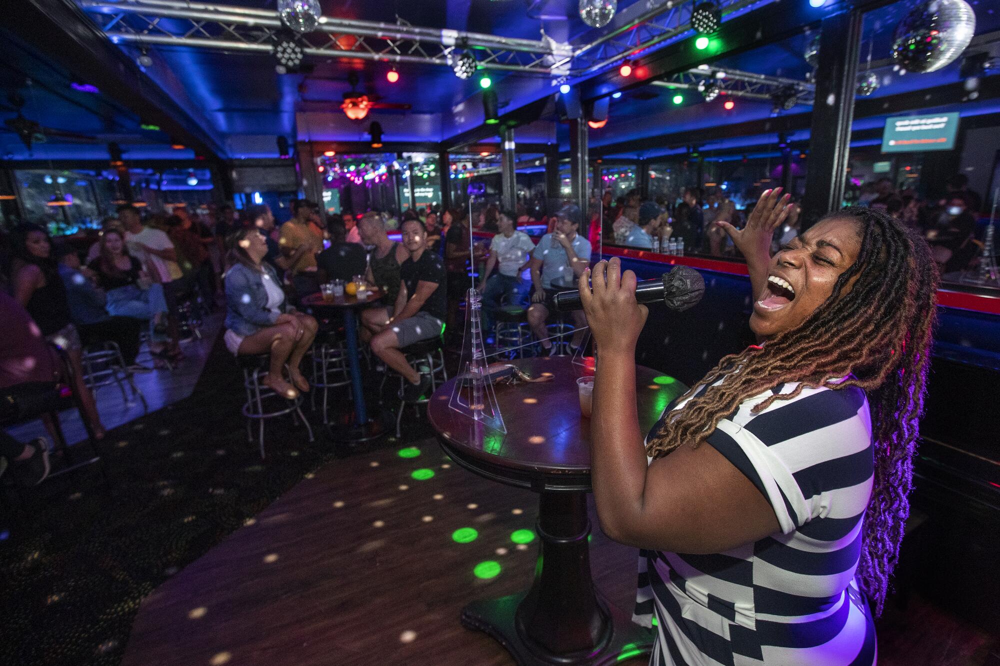 A woman sings karaoke in front of crowd in a dark bar