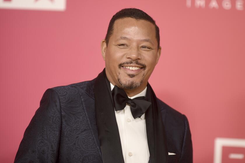Terrence Howard smiles in a black suit and bowtie against a pink backdrop.