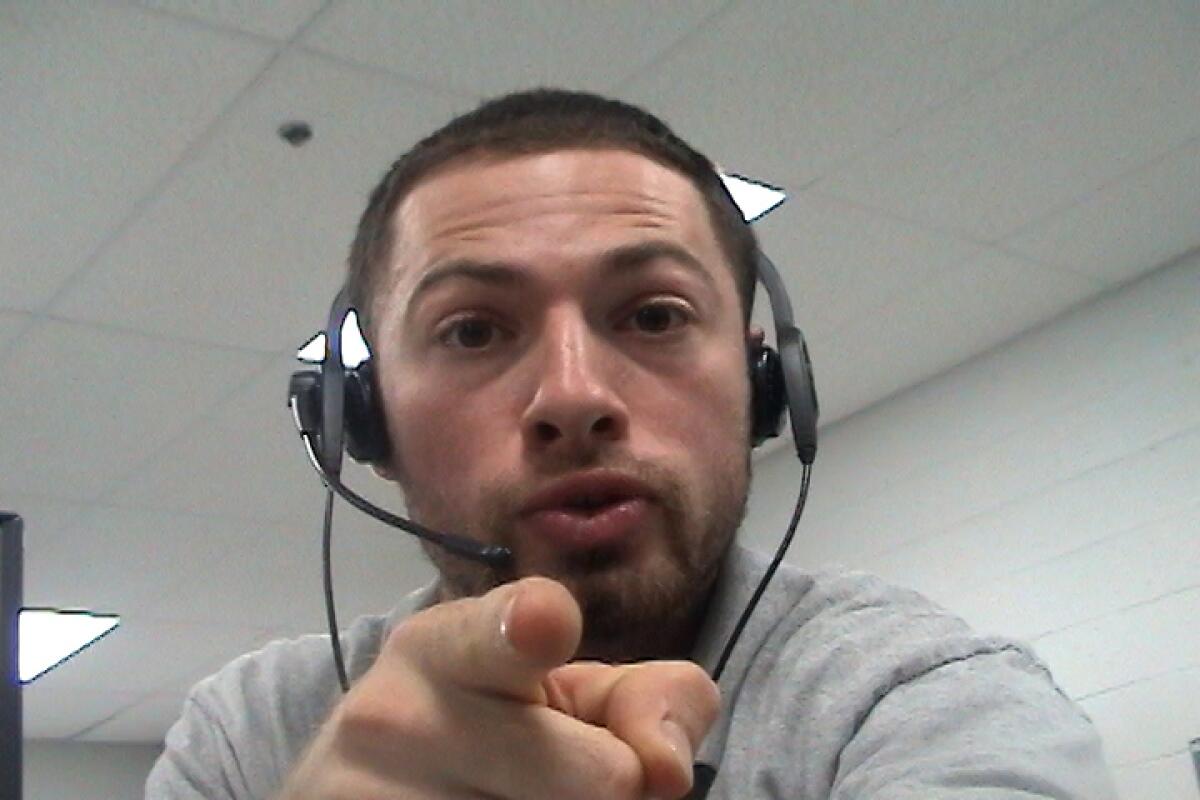 A man wearing a call headset points directly at the camera.