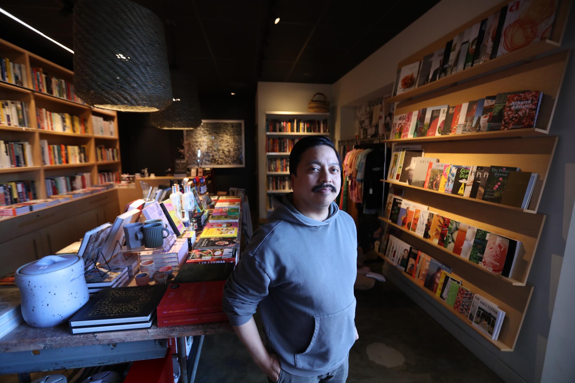 A man in a hoodie poses in the middle of a bookstore.