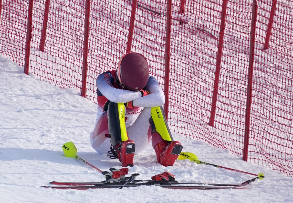 U.S. skier Mikaela Shiffrin sits in the snow with her head buried in her arms, her skis and poles on the ground next to her