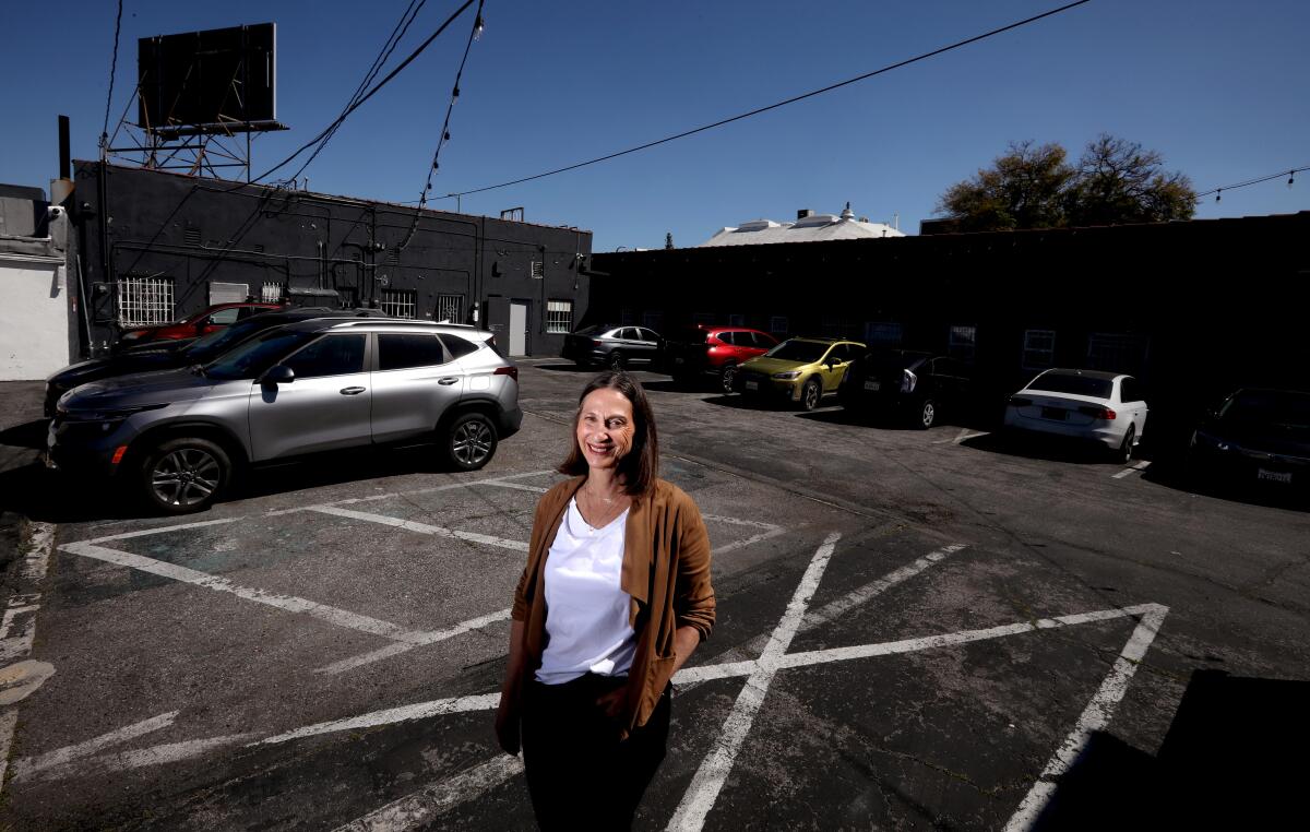 A woman stands in a parking lot near buildings.