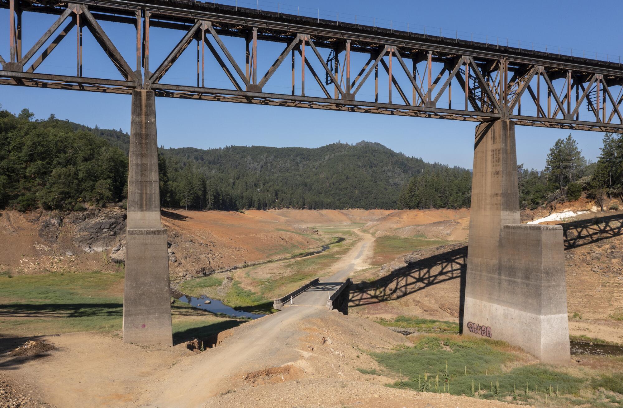 A railroad bridge frames an old roadway, revealed by receding water levels.