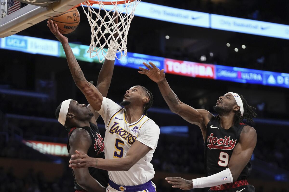 Lakers forward Cam Reddish, center, shoots over Portland Trail Blazers center Duop Reath, left, and forward Jerami Grant.