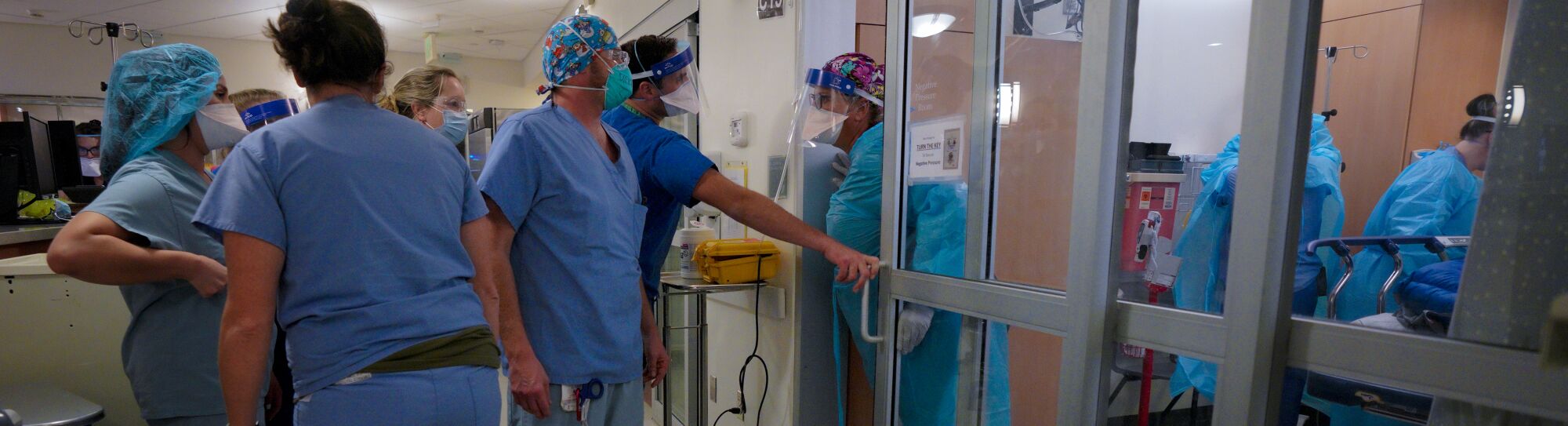 Nurses stand to assist doctors and nurses inside the negative pressure room.
