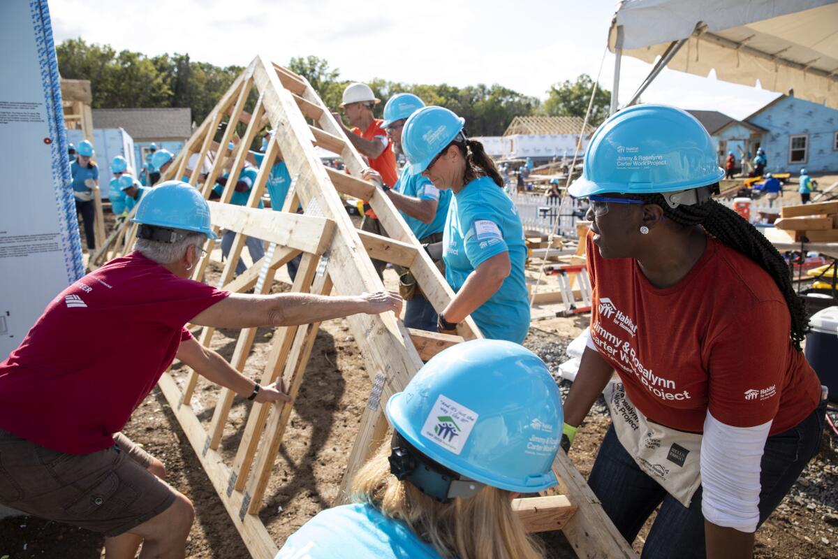 Volunteers in hard harts work on constructing the frame of a house.