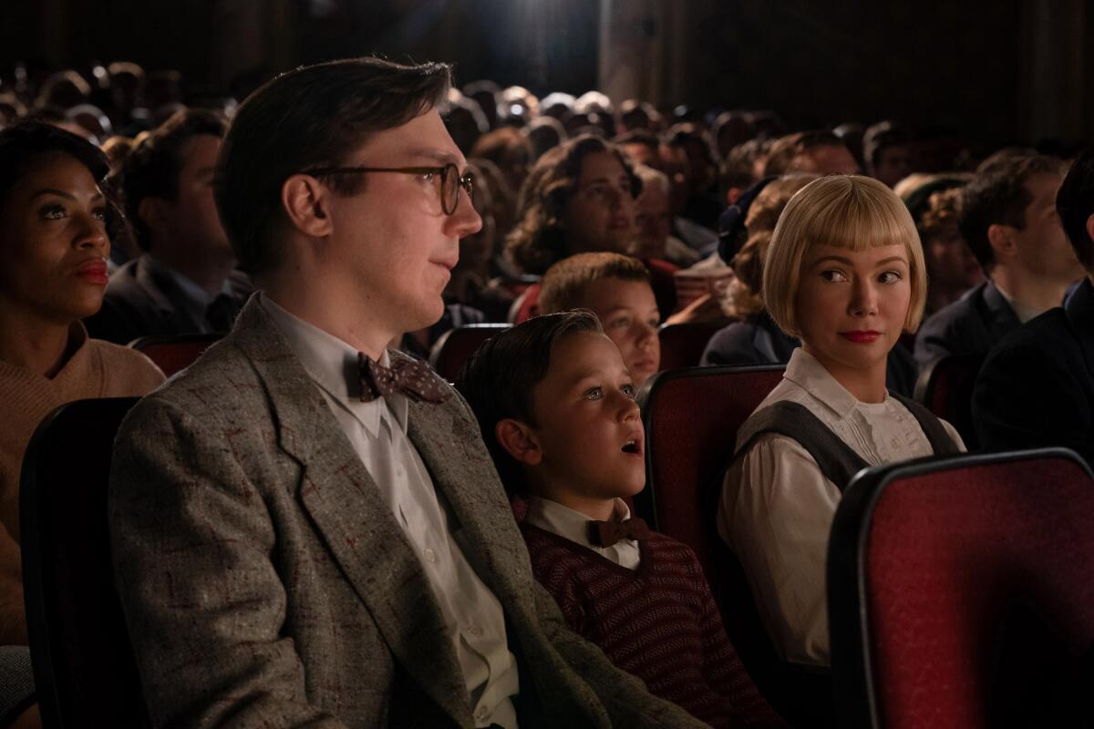 A man and woman flank a small boy entranced by the movie they're watching in a theater in a scene from "The Fabelmans."