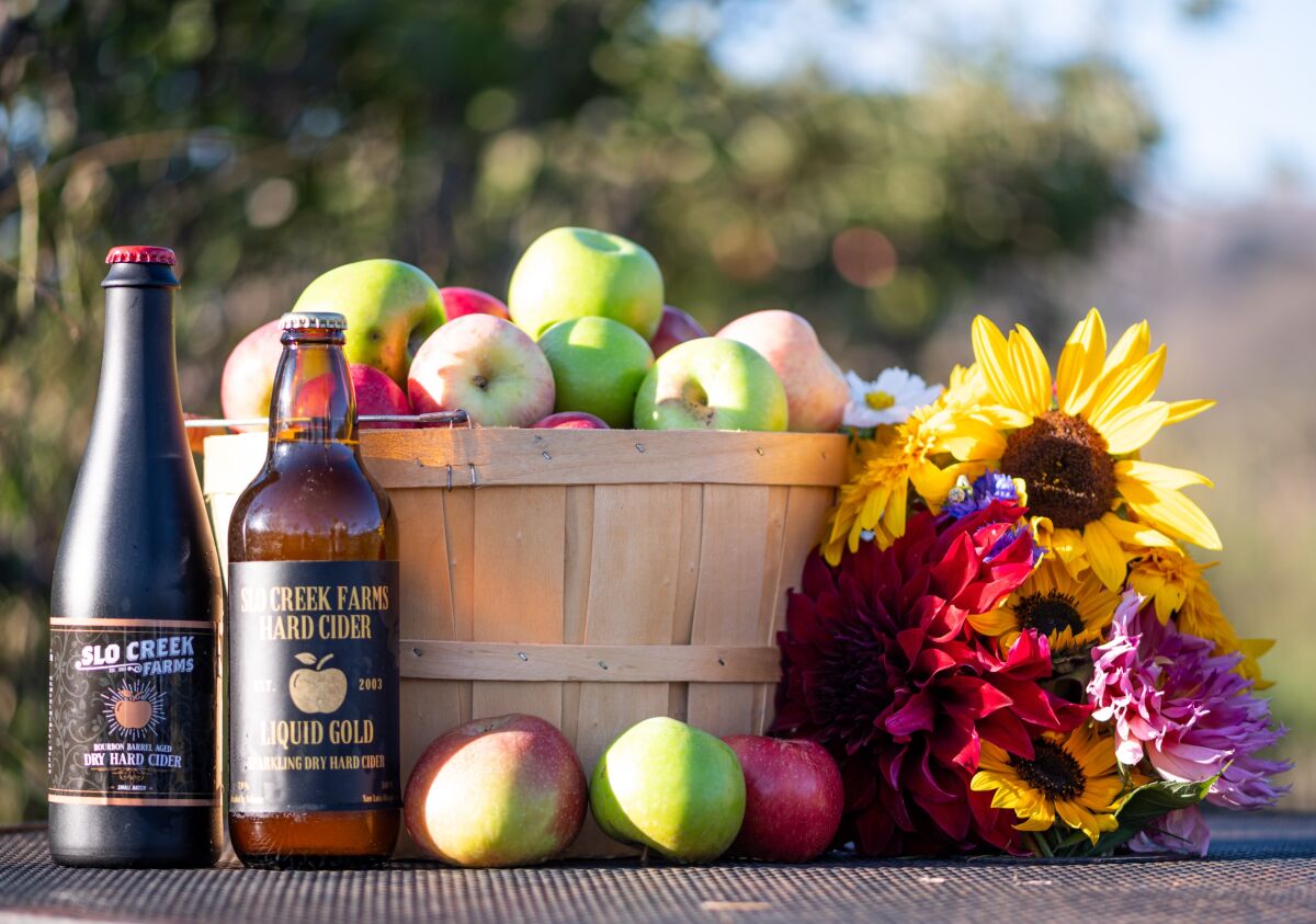 A barrel of apples next to two cider bottles and cut flowers