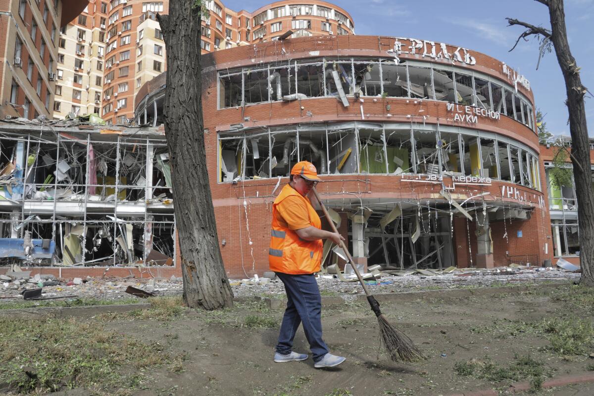 A municipal worker sweeps up debris in front of a building that's had all its windows blown out