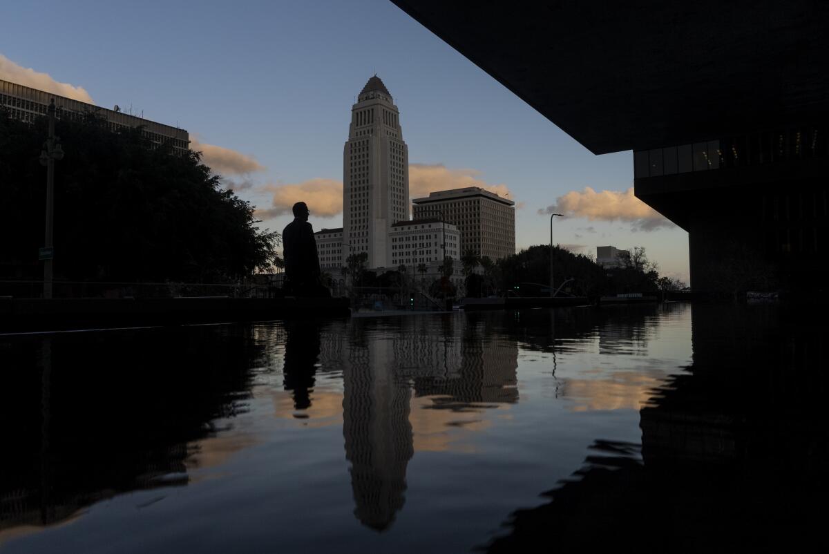 A person in silhouette and L.A. City Hall are reflected in a pool of water