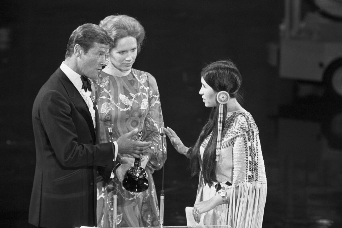 A woman refuses an award from two presenters next to a microphone