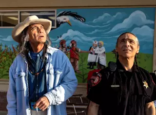 Two men, one in denim and the other in a black police uniform, look upward.