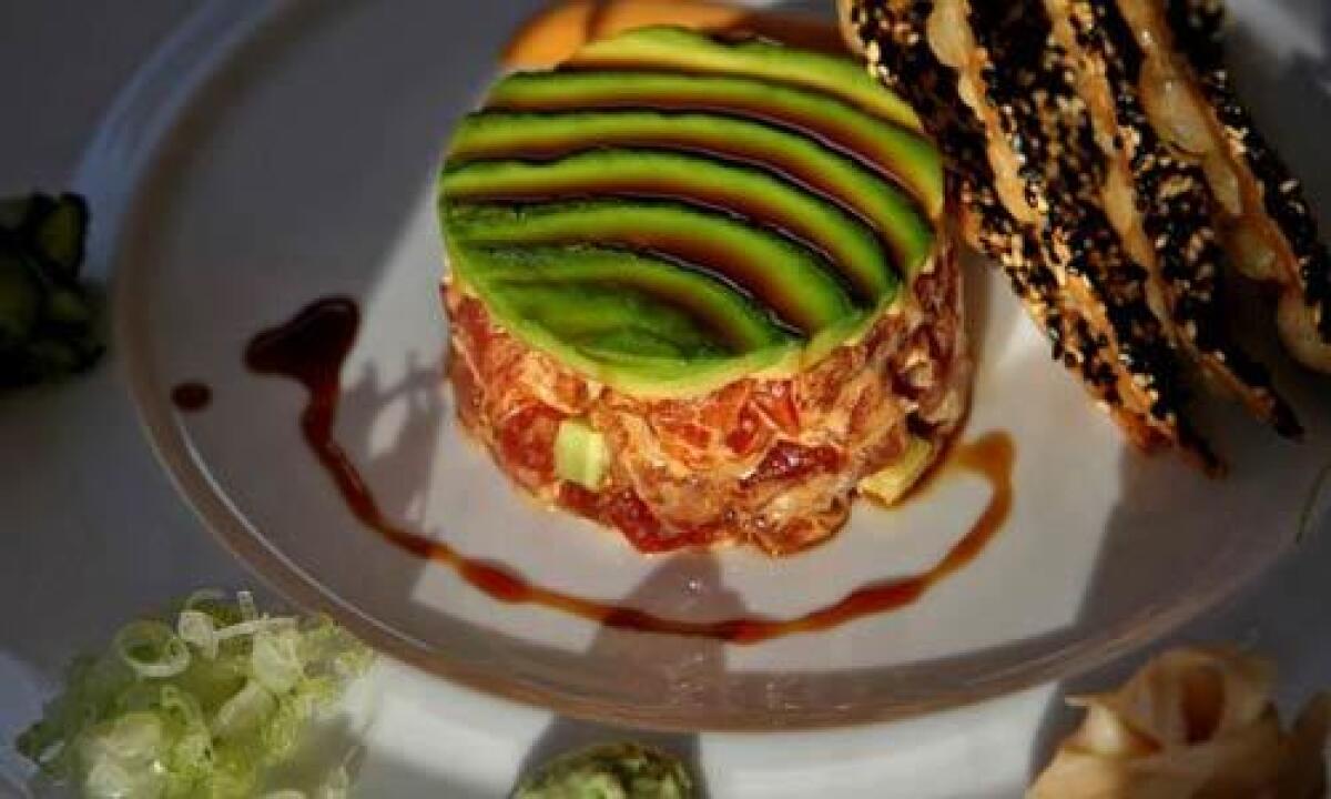 Tuna tartare consists of sashimi grade tuna, hand-cut and presented in the center of the plate with garnishes arranged on the rim. There's pickled cucumber, ginger, wasabi, finely cut scallions and more. It comes with crackers covered in black and white sesame seeds.
