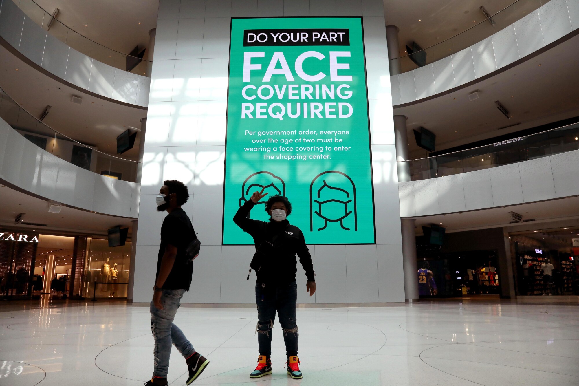 A masked shopper holds his fingers in a peace sign at the Beverly Center.