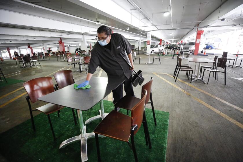 GLENDALE, CA - JULY 28: Janitor Juan Camacho wipes tables clean after diners consumed lunch in the Glendale Galleria parking structure which in a creative effort has set up tables and chairs in the Galleria parking structure to create an outdoor dining area. Glendale Galleria on Tuesday, July 28, 2020 in Glendale, CA. (Al Seib / Los Angeles Times)