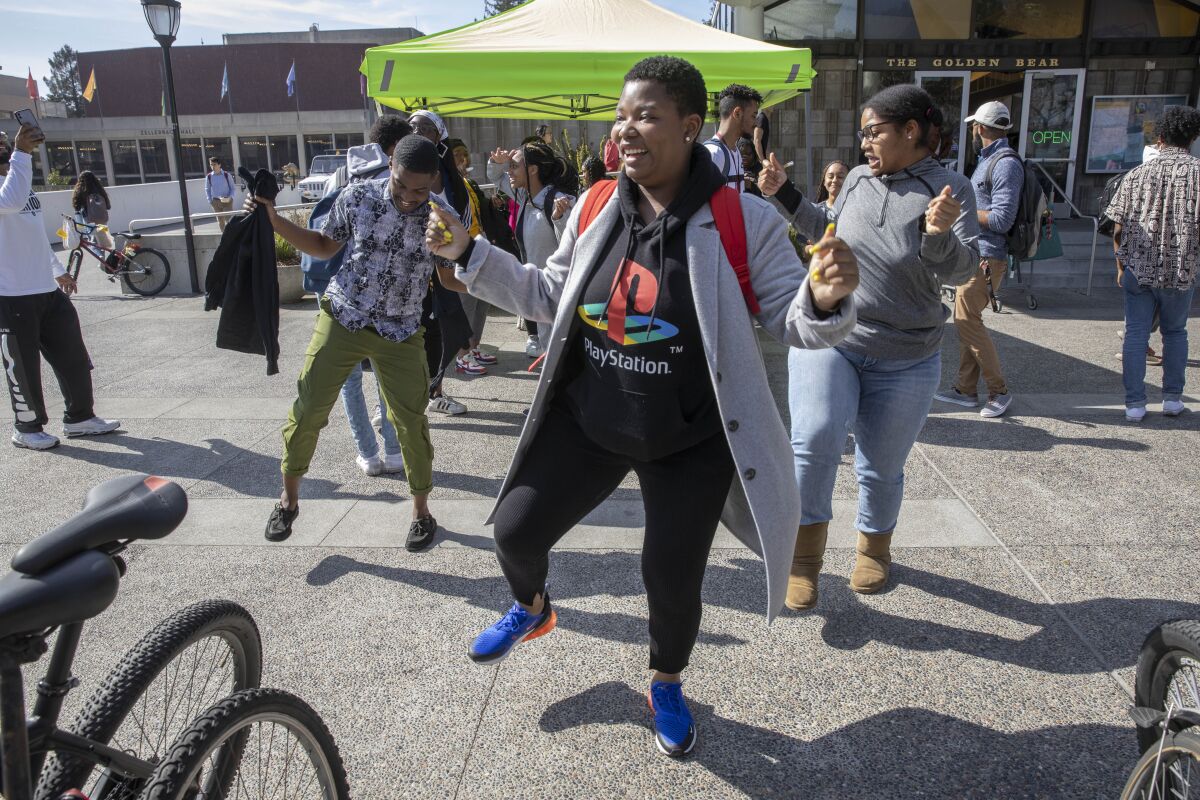 Students dance in front of a pop-up tent in a university plaza