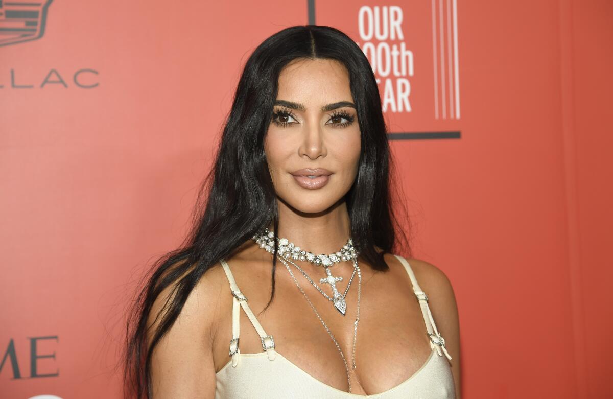 Kim Kardashian poses in a white dress and chunky cross necklace.