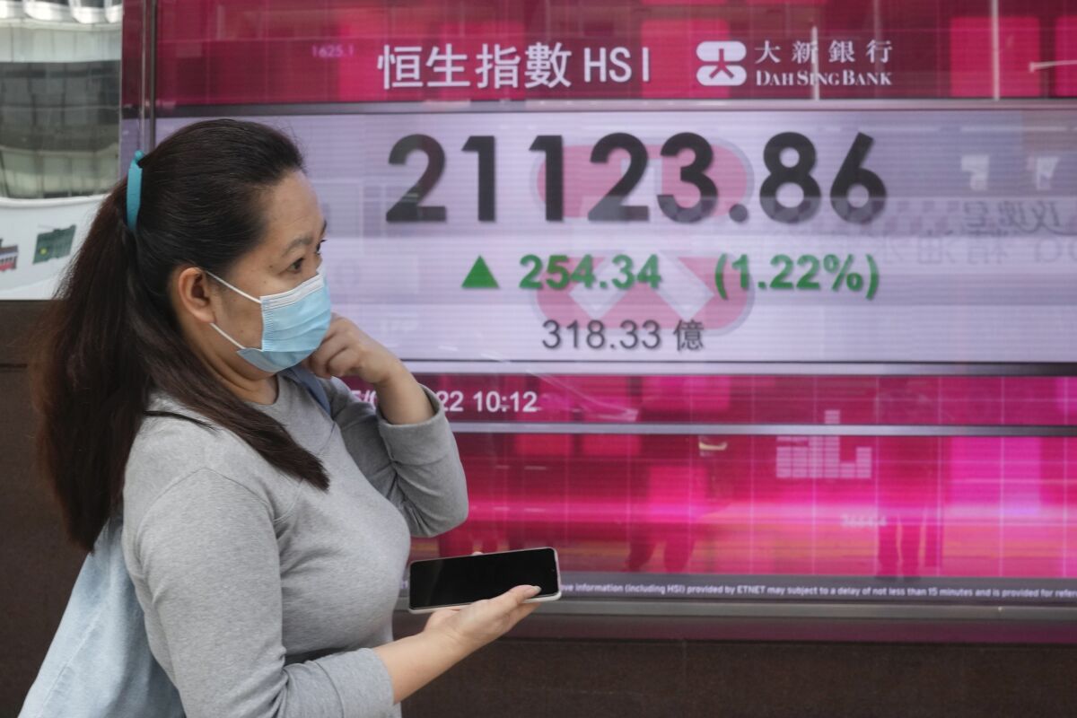 A woman wearing a face mask walks past a bank's electronic board showing the Hong Kong share index in Hong Kong, Thursday, May 5, 2022. Asian stock markets followed Wall Street higher on Thursday after the Federal Reserve chairman downplayed the likelihood of bigger rate hikes following the U.S. central bank's biggest increase in two decades. (AP Photo/Kin Cheung)