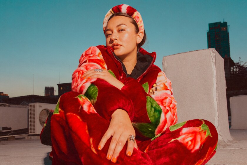 Designer Brenda Equihua sits down on the floor and stares at the camera while wearing a cobija jacket