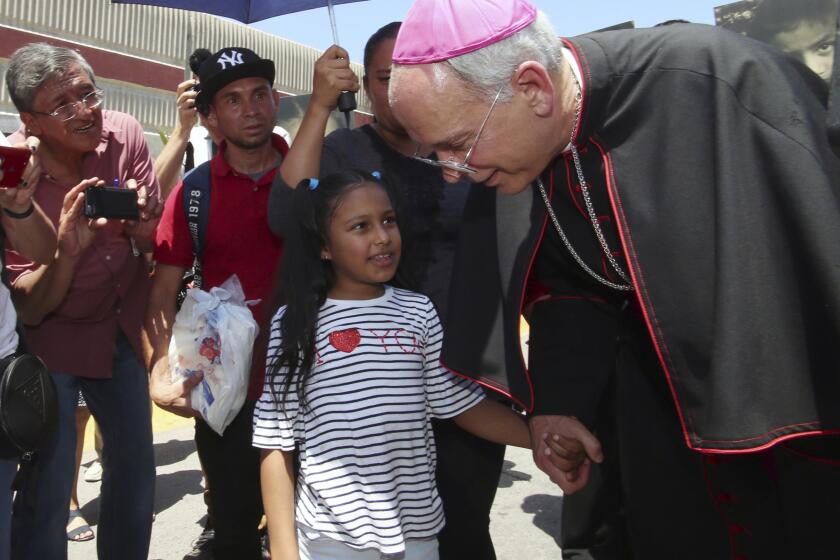 FILE - El Paso Catholic Bishop Mark Seitz talks with Celsia Palma, 9, of Honduras, as they walked to the Paso Del Norte International Port of Entry, Thursday, June, 27, 2019, in Juarez, Mexico. (AP Photo/Rudy Gutierrez)