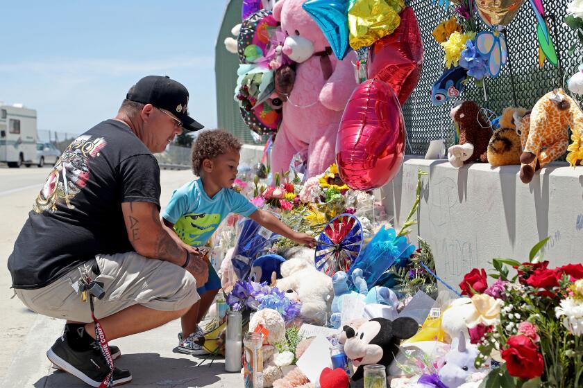 Albert Lamonte of Huntington Beach looks on as his son, Marcel, 2, places a paper pinwheel among a makeshift memorial for 6-year-old Aiden Leos, of Costa Mesa, who was fatally shot during a road rage incident on the 55 Freeway in Orange last week. A $150,000 award is being offered for information leading to the arrest of those responsible for the boys' death.