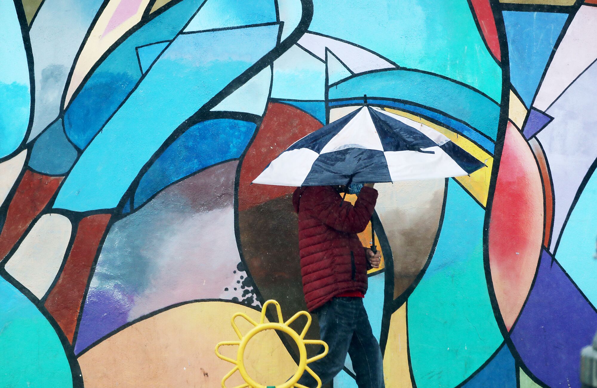 A person with an umbrella in front of a colorful mural.