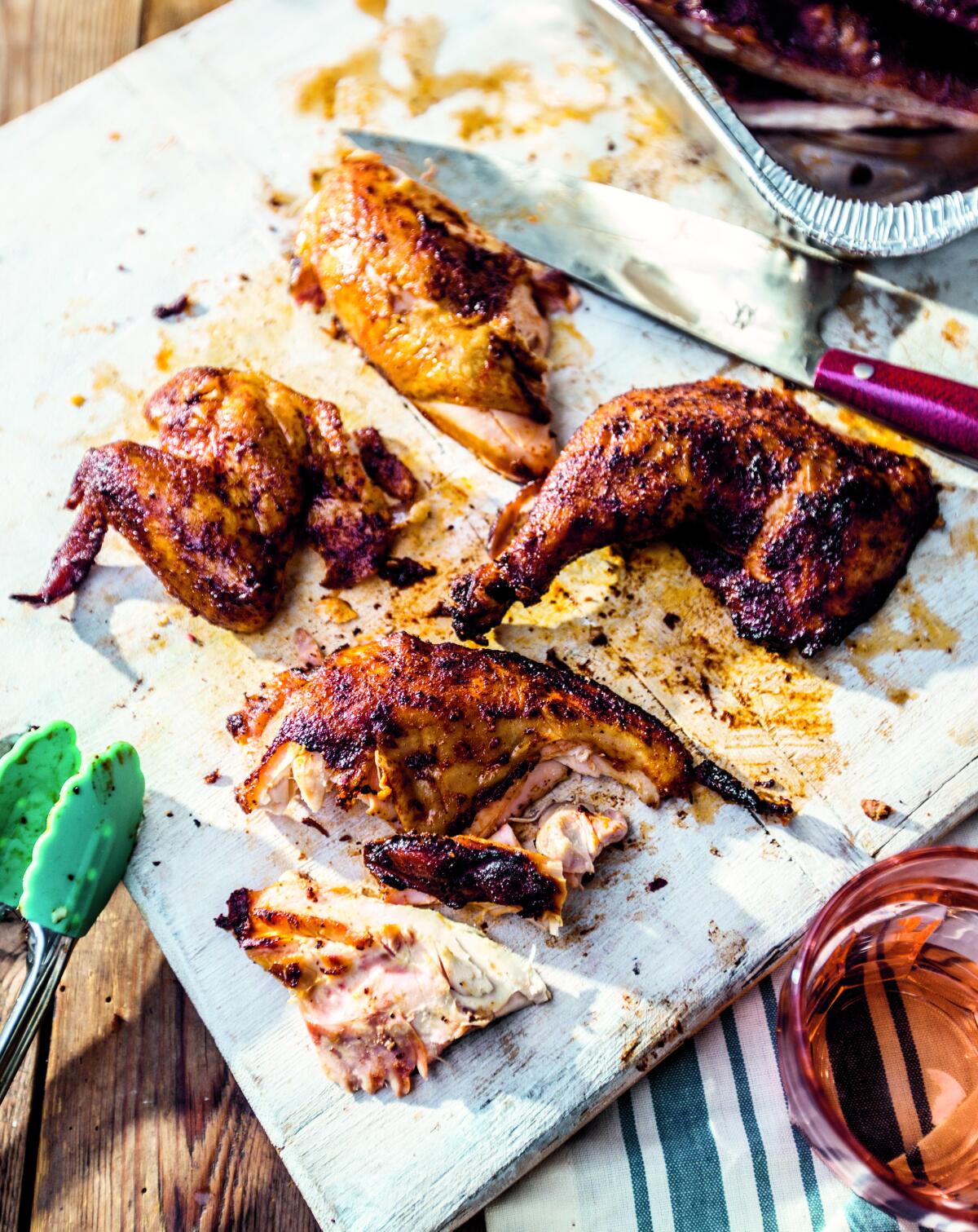 Pieces of smoked chicken are arranged on a cutting board, with tongs and a knife resting on the board. 