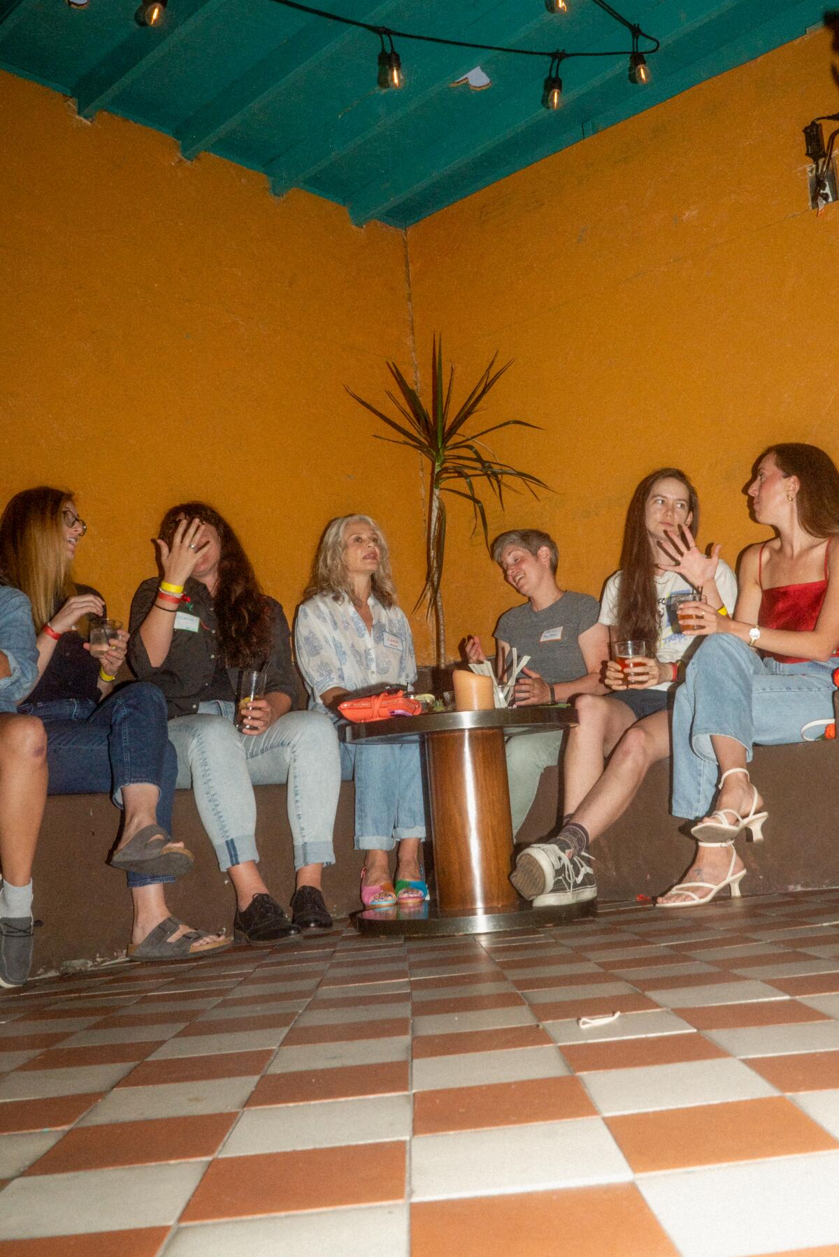 Six people sit in a line in a corner against an orange wall