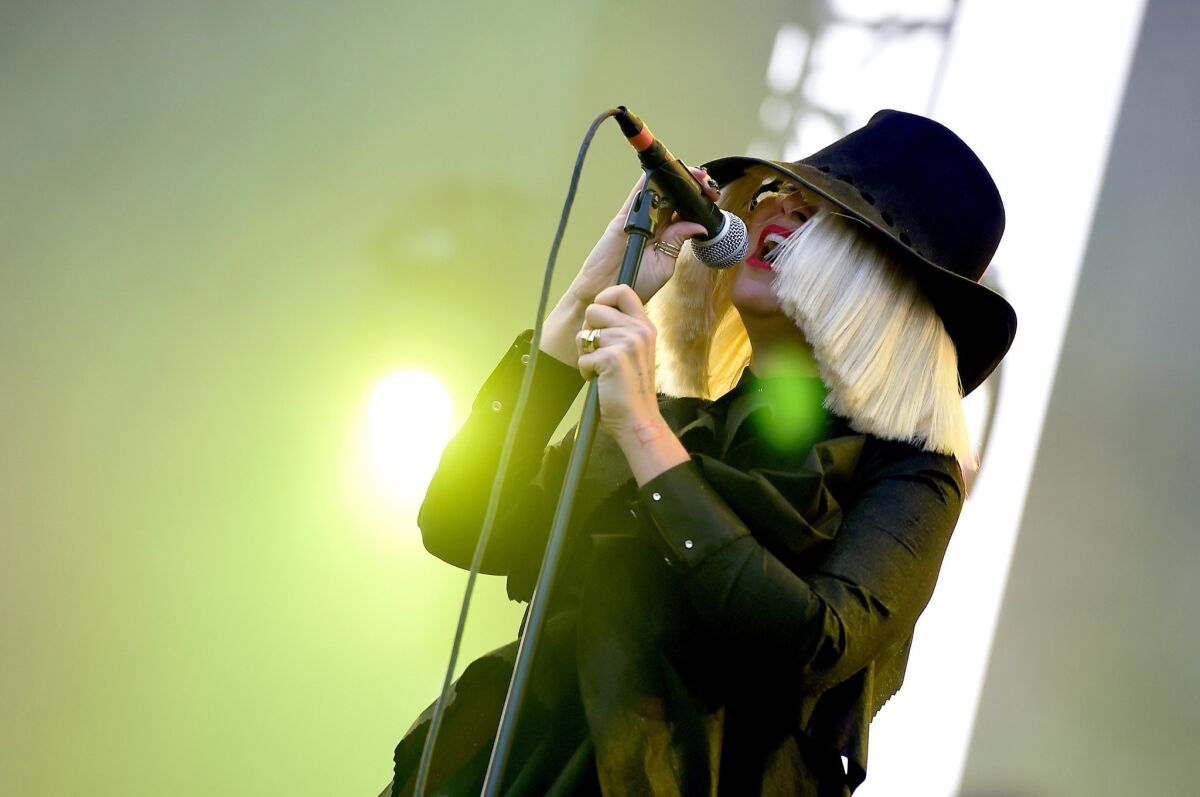 Sia singing while wearing a hat and hair that obscure her face.