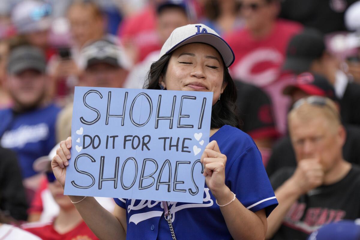 An Ohtani fan with a Dodgers cap and jersey holds a sign reading "Shohei Do It for the Shoebaes" at Great American Ballpark.