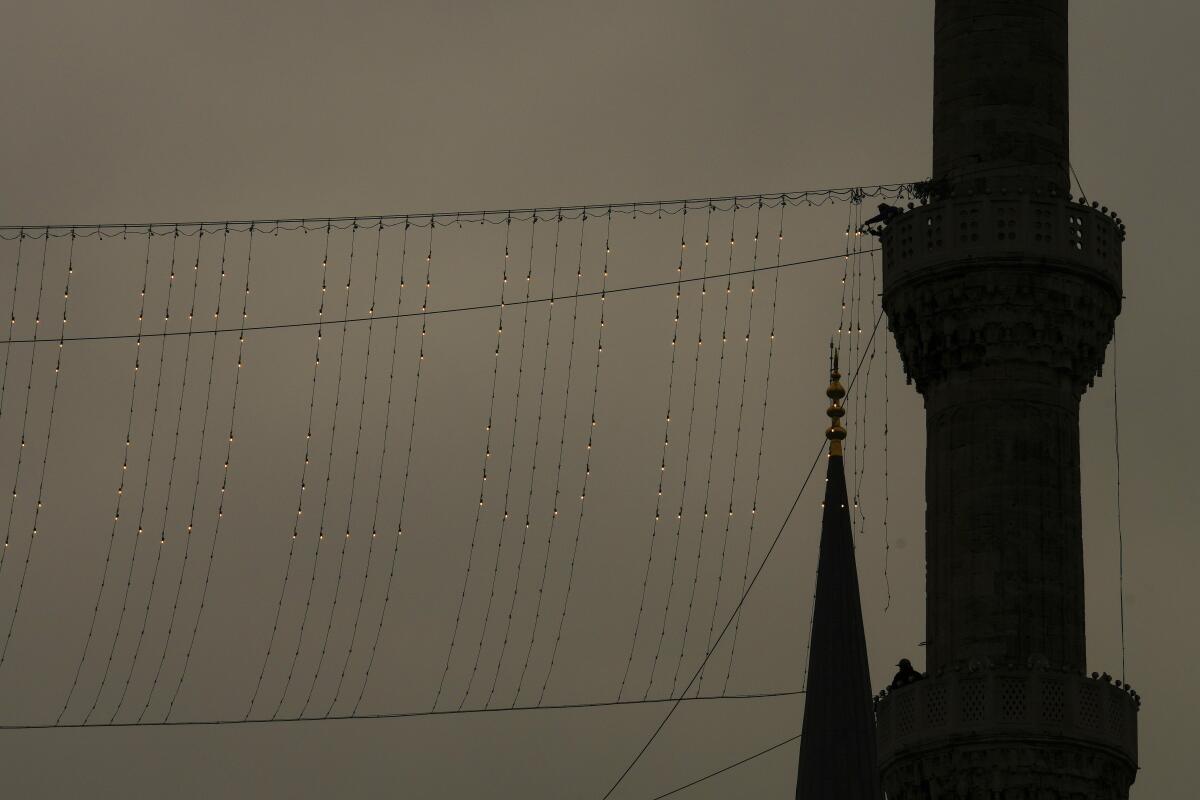 Mahya worker installs light strings between minarets