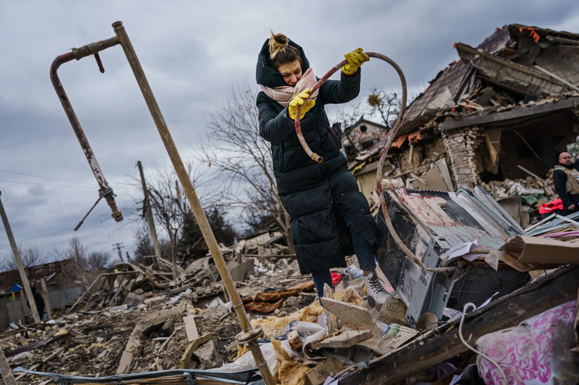 A woman holds up a hose that has red stains on it amid rubble.