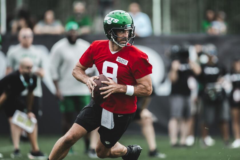 A quarterback in a red jersey with a green Jets helmet.