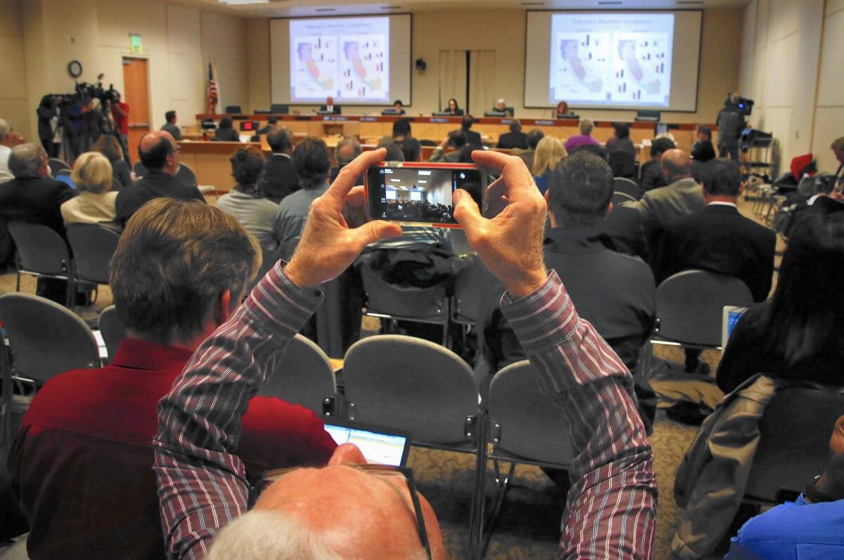 Audience members snap photos of the grim conservation statistics flashing on the screen at a State Water Resources Control Board meeting in Sacramento.