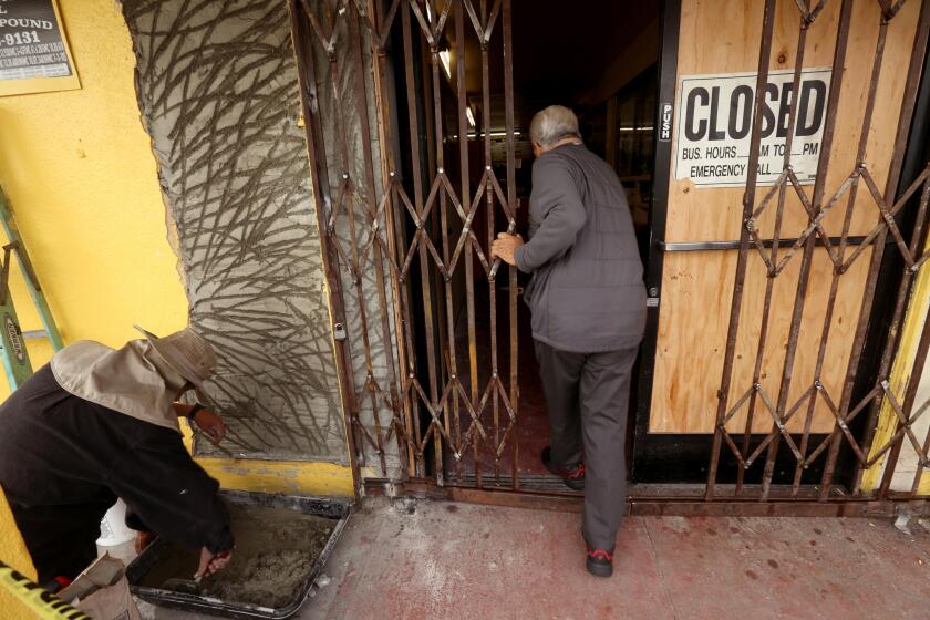 COMPTON, CA - JANUARY 4, 2024 - Ruben Ramirez, Sr., 83, owner of Ruben's Bakery & Mexican Food Inc, walks past a worker who repairs the front door of the family-run business in Compton on January 4, 2024. The store was left ransacked after a street takeover on Tuesday. The mob ran a car through its doors, then stole cash registers and merchandise. No one was hurt, but the family is left devastated with the aftermath. The family lost around $2,000 in cash and about $70 to $80,000 in damage to the store which has been in business for 48 years. (Genaro Molina/Los Angeles Times)