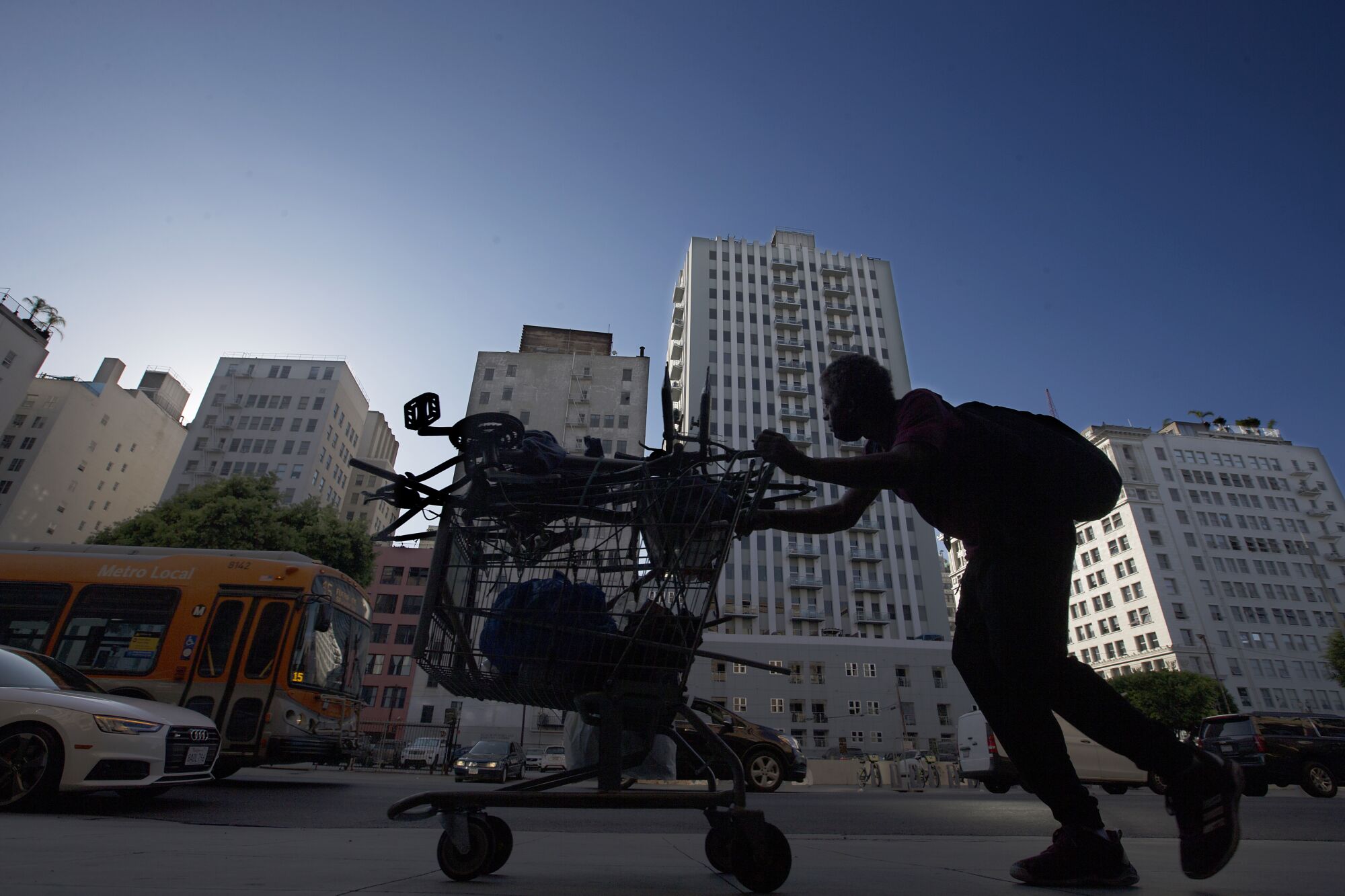 A man pushes a shopping cart along the sidewalk in the historic urban core of Los Angeles.