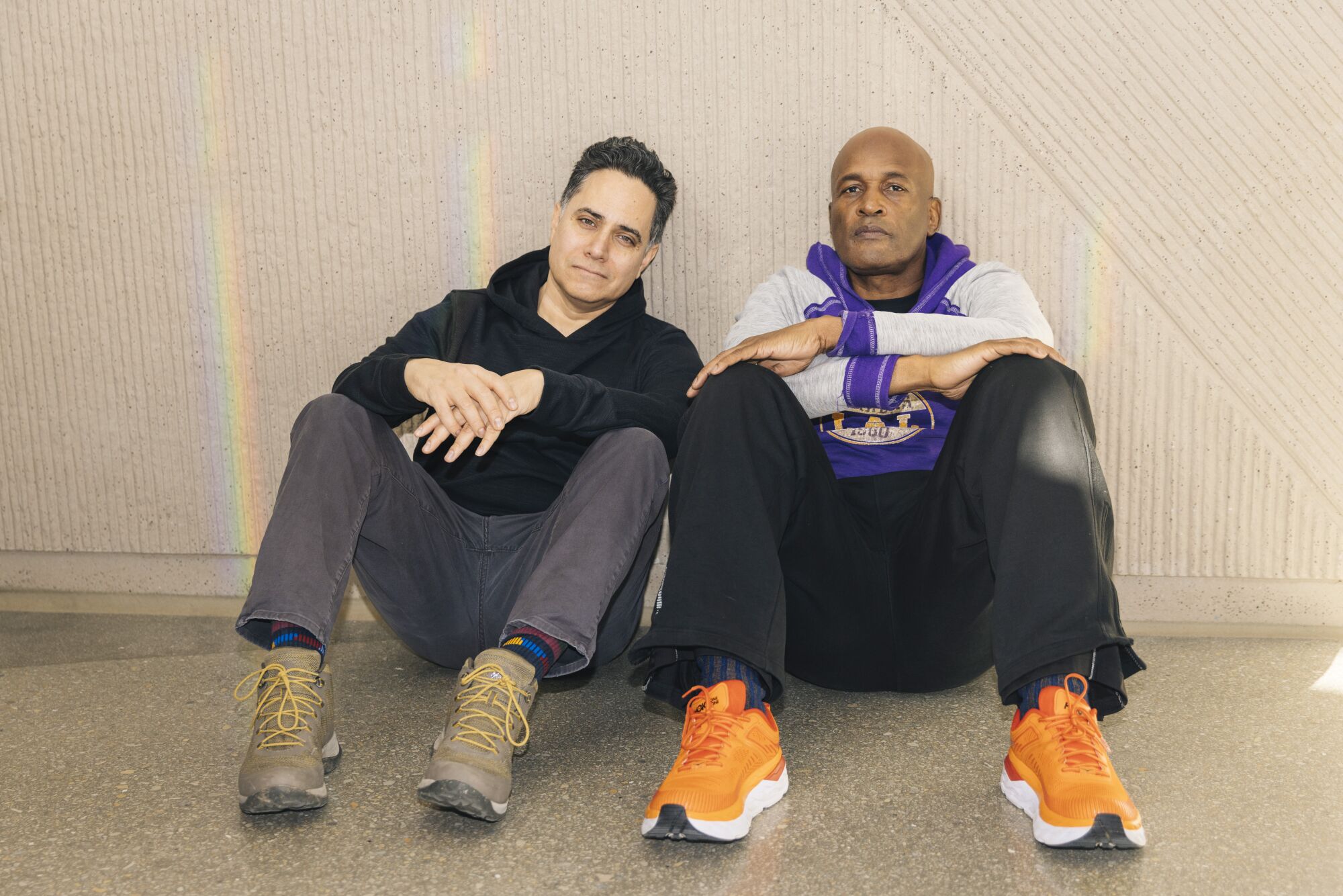Two men sit on the ground, leaning against a wall.  