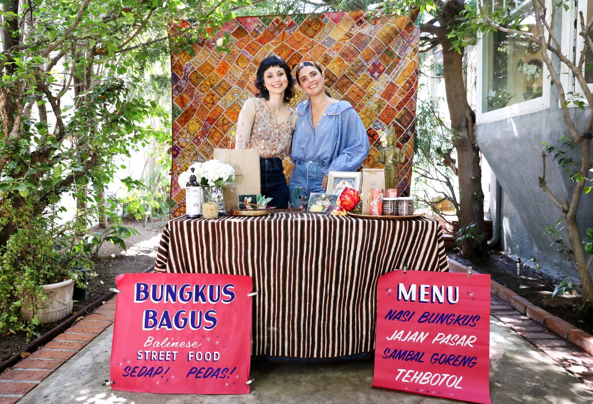Two women stand at a reception table behind a sign that announces "Bungkus Bagus: Balinese Street Food."