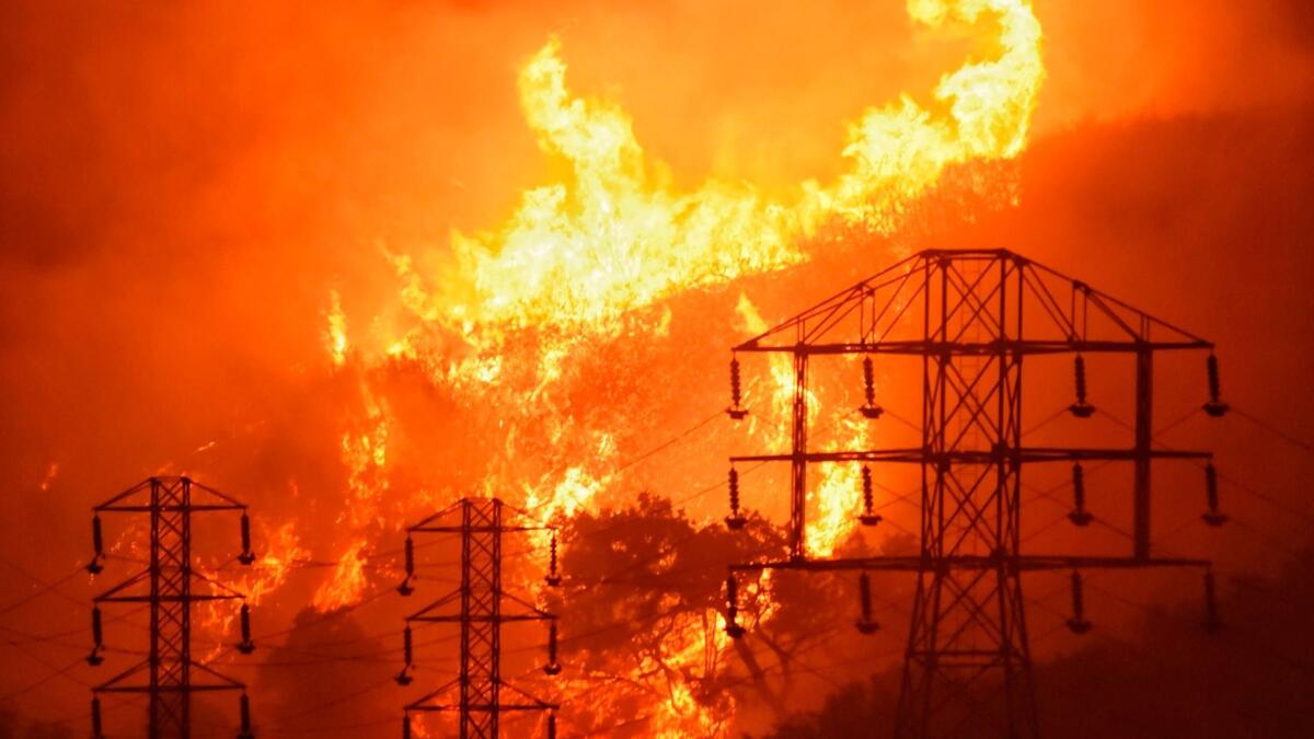In this Dec. 16 photo provided by the Santa Barbara County Fire Department, flames burn near power lines in Sycamore Canyon near West Mountain Drive in Montecito, Calif.