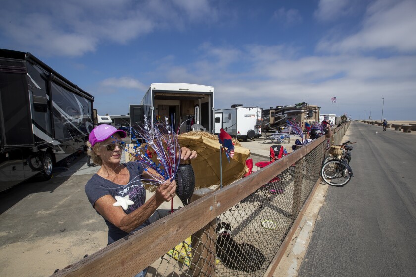 Huntington Beach, CA - May 26: Mark and Tami Burnett, of Lancaster, who's fathers both served in Marine Corps, put up American flag decorations while camping with their dog, Emi, for the Memorial Day getaway weekend at Bolsa Chica State Beach campground in Huntington Beach Thursday, May 26, 2022. (Allen J. Schaben / Los Angeles Times)