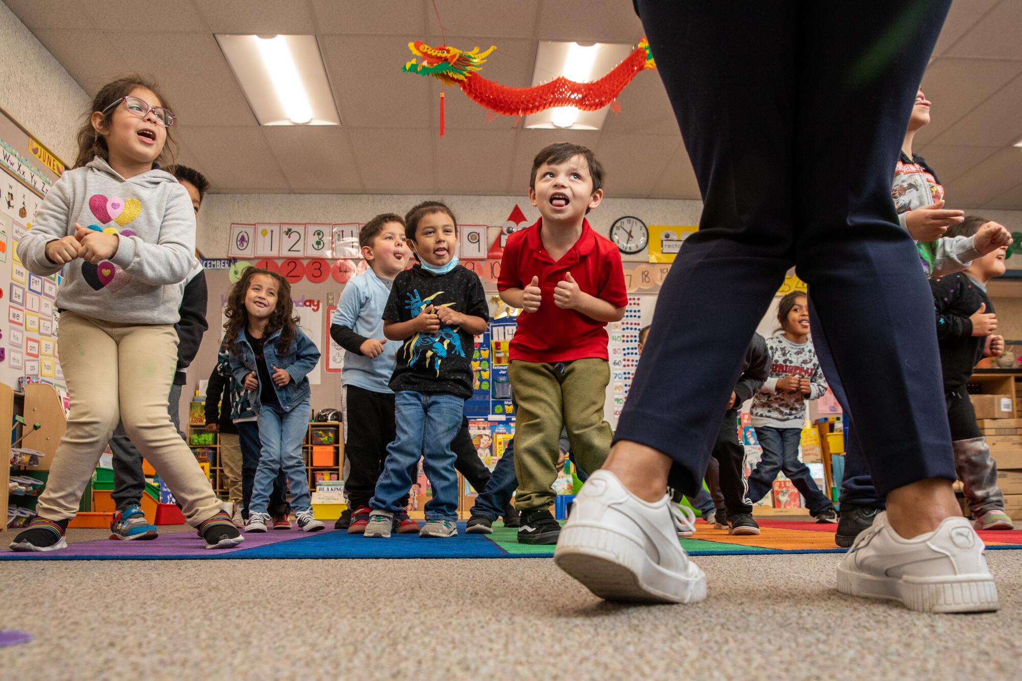 Preschool children stand in class with their teacher. 