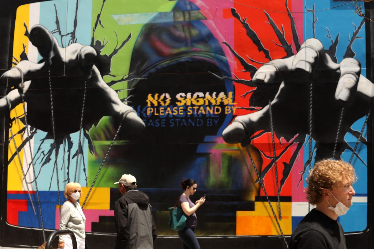 Visitors, some wearing masks, walk past a mural by artist Hijack while visiting the Third Street Promenade.