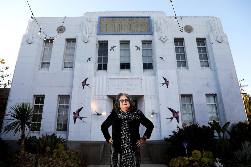 Artist Judy Baca, dressed in black, stands before the Art Deco building that houses SPARC in Venice